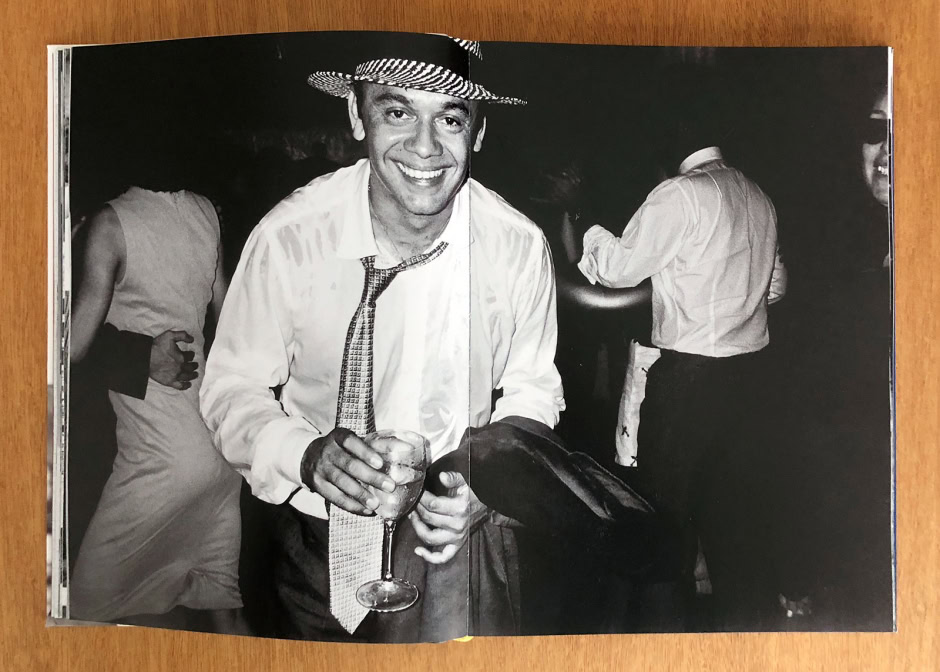 Elegant black and white photograph of a smiling man wearing a hat, tie, and dress shirt holding a drink, capturing a lively moment at a social event or party.