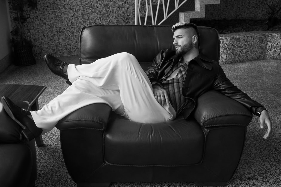 Men fashion photography, black and white portrait of a stylish man lounging on a leather sofa, edgy men's fashion shoot, urban interior background, men's style, men's grooming, fashion photography, contemporary men's portraiture.