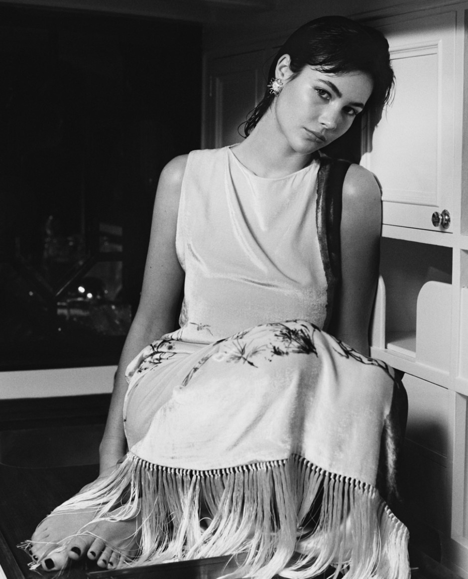 A woman sitting on a chair in a black and white portrait photograph, wearing elegant attire with floral details and fringe, showcasing sophisticated fashion photography by Pamela Hanson.